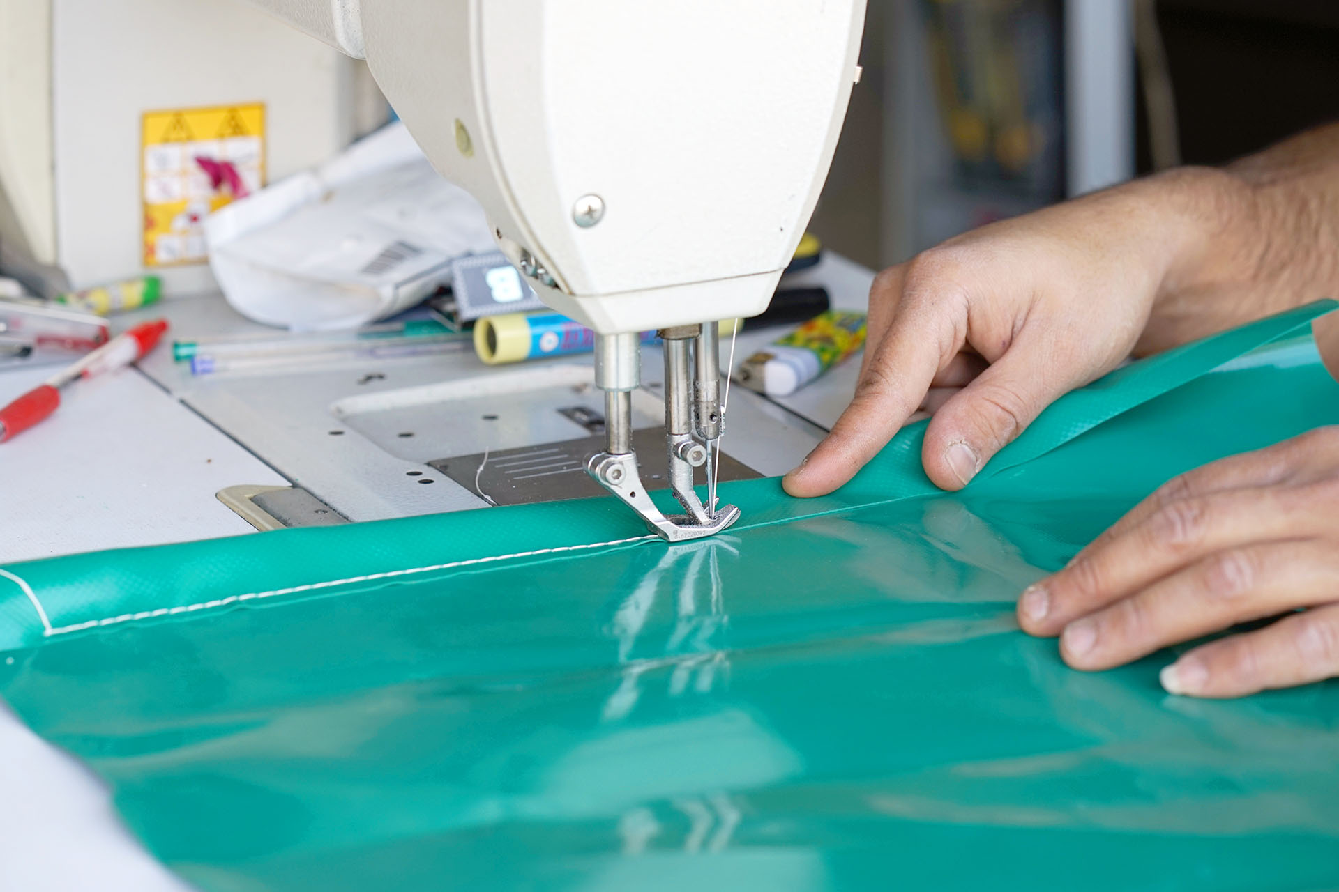a person sewing a part of a green tarpaulin with pens and thread in the bacxkground